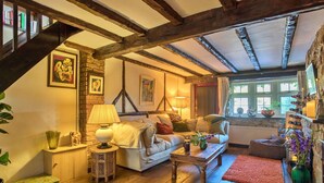 A cozy living room with exposed wooden beams, a fireplace, a stone wall, and a bookshelf. - Stunning  villa for 4 people with WIFI and pets allowed (Felbridge)