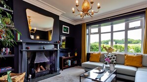 A living room with a fireplace, a sofa, a coffee table, and a large window with a view of greenery.