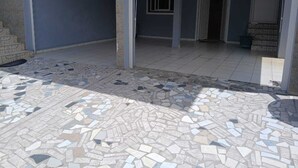 A covered outdoor area with a tiled floor and a partially open door leading to an interior space. - Apartment T3 with swimming pool and garden for your vacations in Guadeloupe (Baie-Mahault)