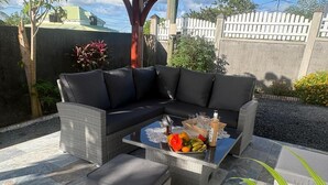 A corner sectional sofa with a matching ottoman and a glass coffee table with fruits and a bottle. - Apartment T3 with swimming pool and garden for your vacations in Guadeloupe (Baie-Mahault)