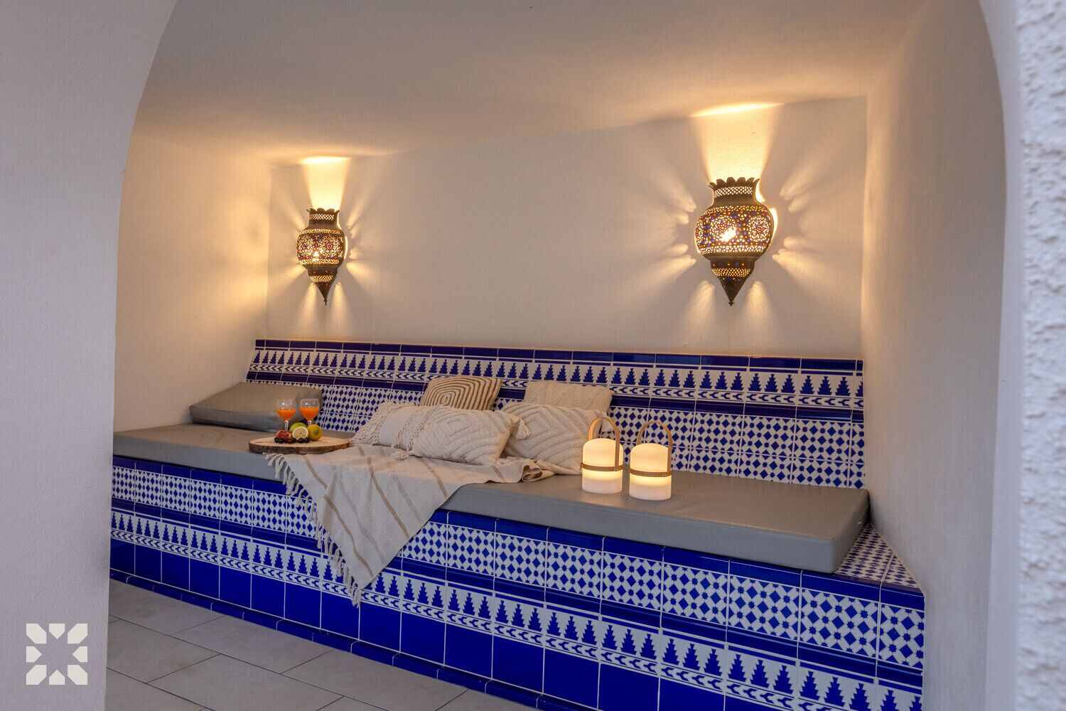 A cozy room with a low bed, decorative wall sconces, and a blue patterned tile backsplash.