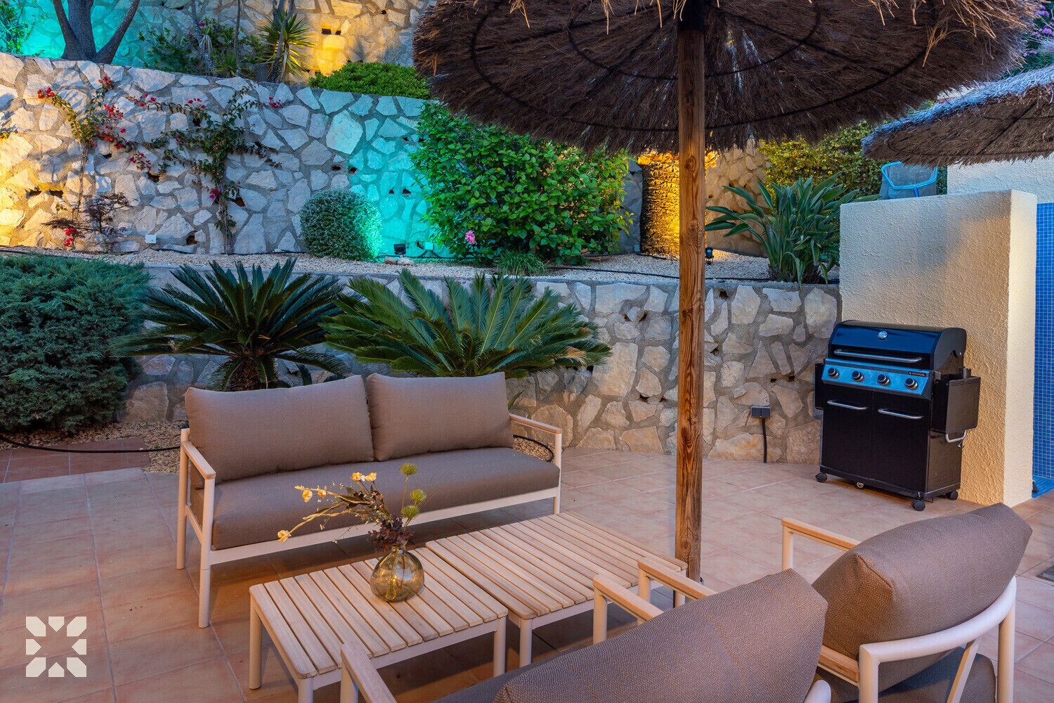 Un patio al aire libre con pared de piedra, un banco de madera, un sofá y una parrilla.