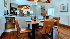 A modern kitchen with wooden beams, a dining area with leather chairs, and a view of the kitchen. - Beautiful  villa for 4 guests with WIFI and terrace (Edlingham)