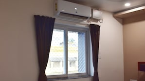 Ett hotellrum med ett fönster, gardiner, en luftkonditioneringsanläggning, ett sängbord och en säng.