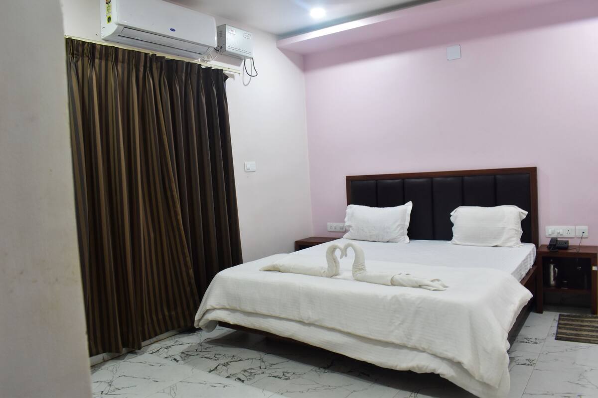 Une chambre d’hôtel avec un lit, une table de chevet, un climatiseur fixé au mur et un rideau.