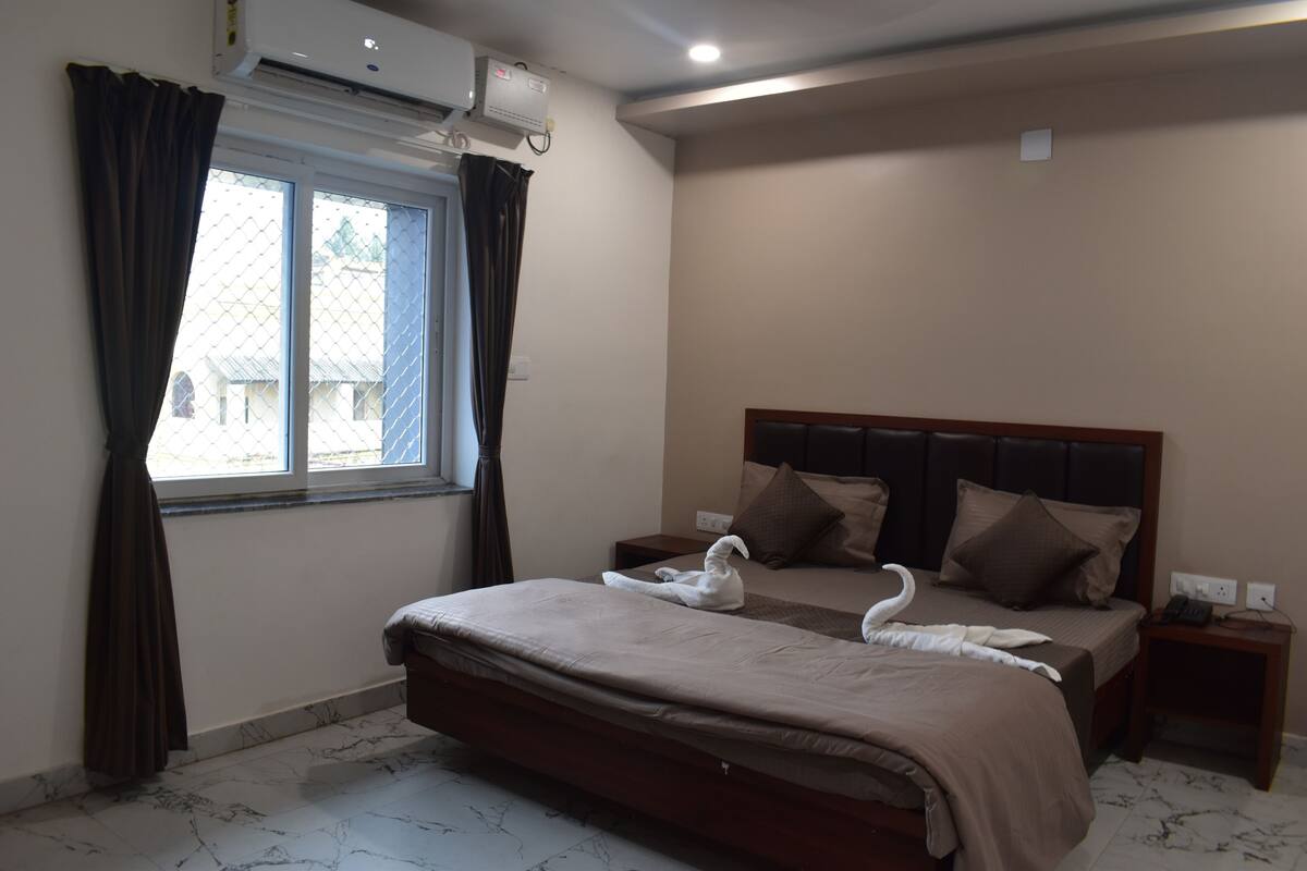 Une chambre d’hôtel comprenant un lit, une table de chevet, une fenêtre avec des rideaux et un appareil de climatisation.