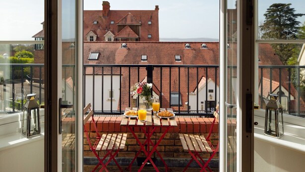 A balcony with a table set for breakfast, including croissants, juice, and a flower arrangement. - Lovely apartment for 5 guests with pool, WIFI, TV and balcony (Tenby)