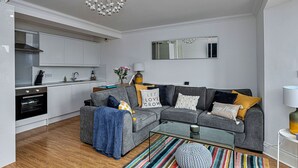 A modern living room with a grey sofa, a glass coffee table, and a colorful striped rug. - Lovely apartment for 5 guests with pool, WIFI, TV and balcony (Tenby)