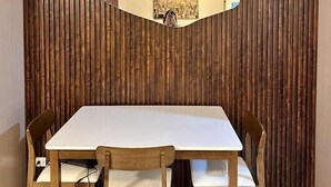 Un comedor con un panel de madera en la pared, una mesa blanca y cuatro sillas de madera.