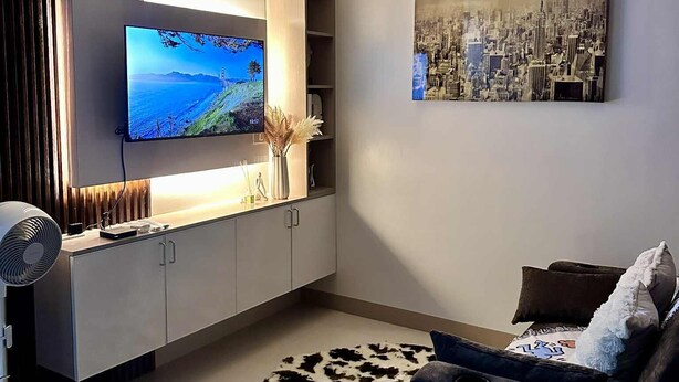 Una sala de estar moderna con un televisor de pantalla plana, un cuadro de paisaje urbano, un tapete de cuero de vaca y un sofá oscuro.