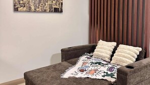 Una sala moderna con un sofá, un cuadro de un paisaje urbano, pared de paneles de madera y una manta estampada.