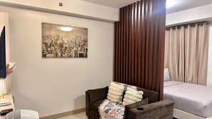 Un dormitorio moderno con un cuadro de paisaje urbano, un sofá marrón con una manta, una cama con cortinas color beige y una alfombra estampada.