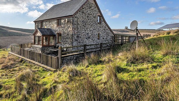 Een stenen huis met een schuin dak, een houten terras en een schotelantenne.