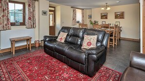 Een woonkamer met een leren bank, een eettafel en een rood tapijtend.
