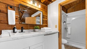 A modern bathroom with a wooden ceiling, a marble sink, a mirror, a potted plant, and a walk-in shower.