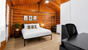 A room with a bed, bedside table, lamp, and a desk with a chair.