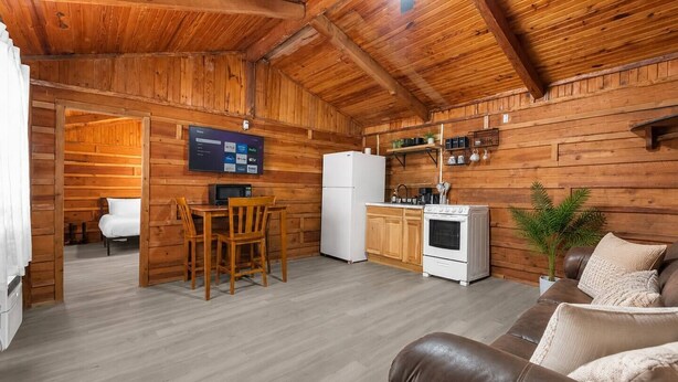 A cozy cabin interior with a wooden interior, a dining area with a table and chairs, a kitchenette with a stove and refrigerator, and a living area with a sofa.
