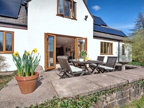 Ein weißes Haus mit Terrasse, Solaranlage und einem Garten mit Narzissen.