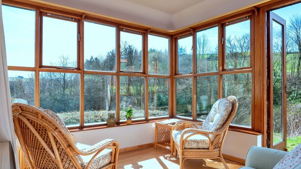 A sunroom with large windows, wicker furniture, and a view of the surrounding trees.