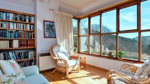 A cozy reading nook with a large window, wicker furniture, and a bookshelf filled with books.