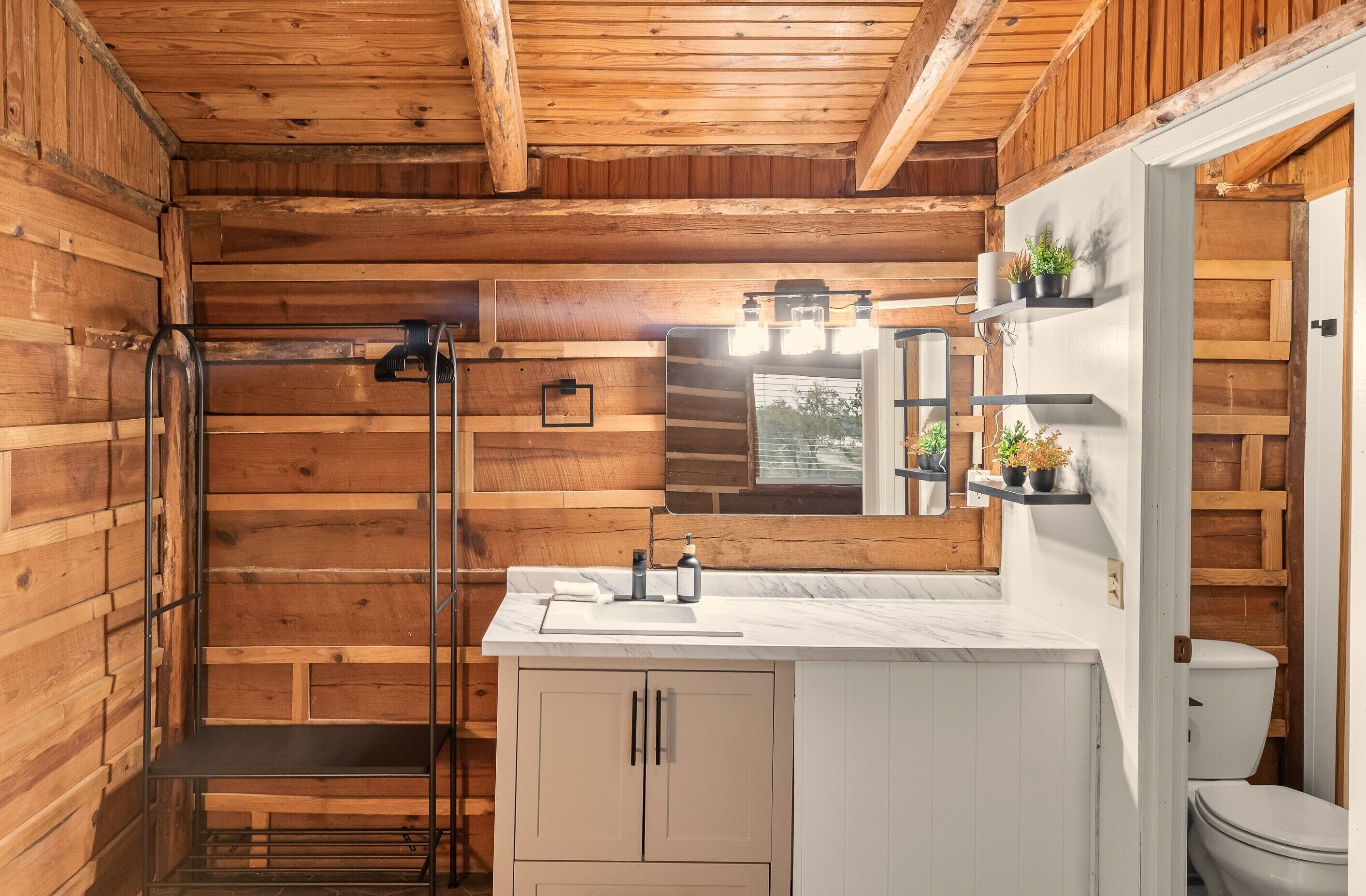 A wooden cabin bathroom with a shower, toilet, and a sink with a mirror.