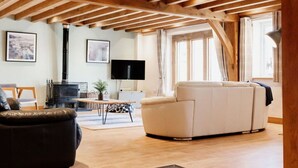 Un salon spacieux avec des poutres apparentes, une cheminée, un canapé et un téléviseur.