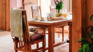 A dining area with a wooden table set for breakfast, including a vase of flowers, a teapot, and a pitcher of juice.