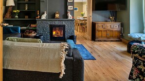 A cozy living room with a fireplace, a sofa, a wooden cabinet, and a dining area in the background.