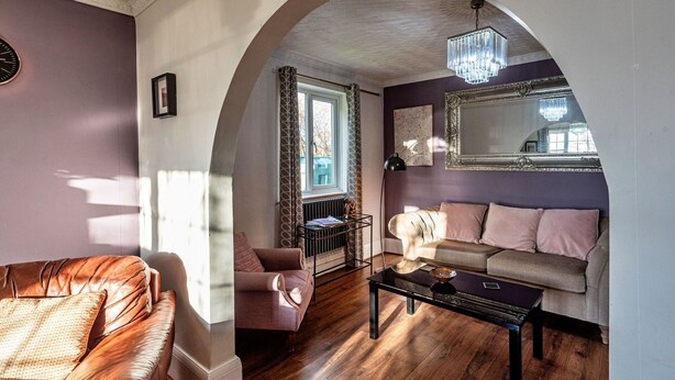 Ein Wohnzimmer mit einem braunen Ledersofa, einem rosa Sessel, einem schwarzen Couchtisch und einem Kamin.