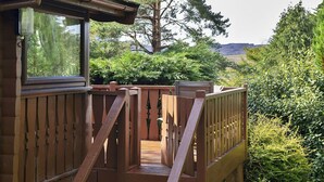 A wooden deck with a staircase leading to a window overlooking a lush garden and a large tree.