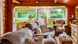 A cozy log cabin interior with a sofa, armchairs, and a dining area.