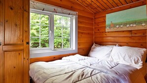 A wooden cabin room with a bed, a window, and a painting on the wall.