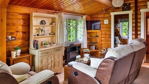 A cozy cabin interior with a leather sofa, wooden shelves, and a television.