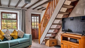 Ein gemütliches Wohnzimmer mit einer Couch, Fernseher, Holzschrank und einer Treppe.