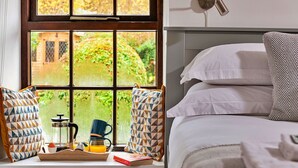 Ein Schlafzimmer mit Fensterbank, Nachttisch mit Kaffeekocher, Tassen und einem Buch.