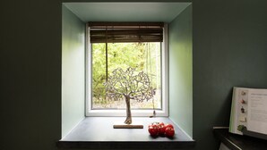 A window with a decorative tree, a clock, and a book on a windowsill.