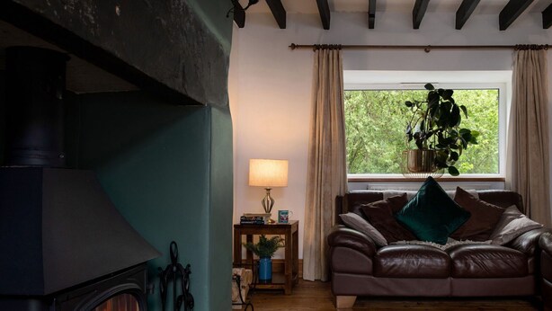 A cozy living room with a fireplace, leather sofa, and a window with a view of greenery.