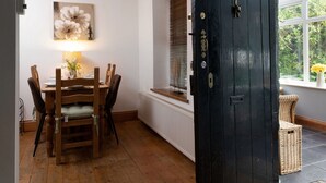 A dining area with a wooden table and chairs, a painting on the wall, and a black door with a window above it.