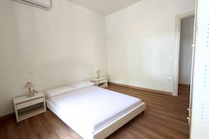 A bedroom with a single bed, two bedside tables, and a door leading to another room. - CV016 - Cervia, new three-room apartment with parking space 100m from the sea (Cervia)