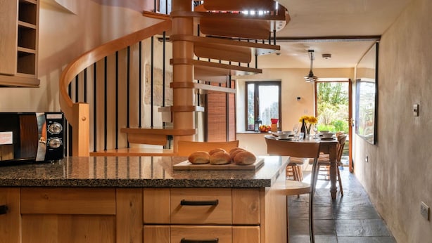 Una cocina moderna con una isla de madera, una escalera de caracol y un comedor con vistas a la vegetación.