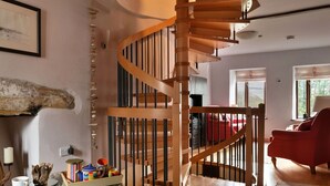 Una escalera de caracol de madera en una sala de estar con una silla roja y una mesa de centro de vidrio.