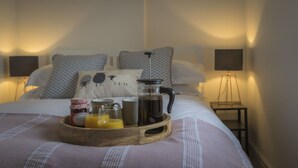 Una cama bien hecha con una bandeja de madera que sostiene una cafetera, tazas y vasos de jugo de naranja.