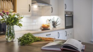 Una cocina con armarios blancos, una estufa y una encimera con un libro y verduras.