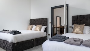 A hotel room with two beds, each with a dark headboard and white bedding. There are folded towels on the beds and a wooden door leading to another room.
