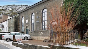 A brick building with arched windows and a stone facade, adjacent to a snow-covered street.
