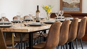 A dining table set with plates, glasses, and a bottle of wine, surrounded by leather chairs.