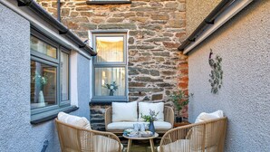 A cozy outdoor seating area with wicker chairs and a table, set against a stone wall with windows. - Wonderful  villa for 6 guests with WIFI, terrace and pets allowed (Ffestiniog)
