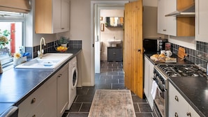 A modern kitchen with a washing machine, a sink, a stove, and a dining area with a table and chairs. - Wonderful  villa for 6 guests with WIFI, terrace and pets allowed (Ffestiniog)