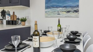 Una cocina moderna con una mesa de comedor dispuesta para una comida, que incluye botellas de vino, cuencos y cubiertos.