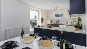 Una cocina moderna con encimeras blancas, un salpicadero negro y un comedor preparado para seis personas, con copas de vino y cuencos.